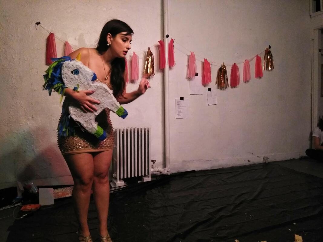 Jenna Kline, Parallel Performance Space, 2019, photo credit Polina Riabova. Female performer in gold studded coctail dress holds a white pony piñata.