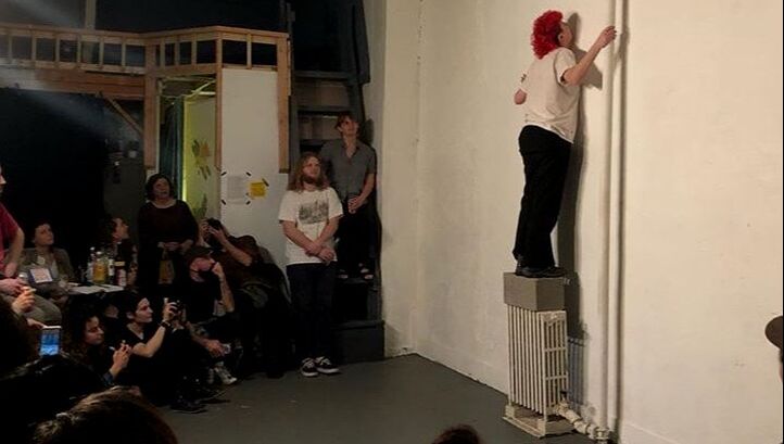 Esther Neff, Parallel Performance Space, 2019. Performance Artist Esther NEff stands on top of a radiator with back to the audience.