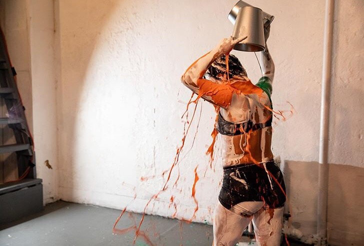 Salomé Egas, Parallel Performance Space, 2019. Performance artist shows back of their body while dumping orange paint over their head.